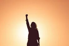Foto: Silhouette einer Person mit erhobenem Arm vor einem Sonnenuntergang.