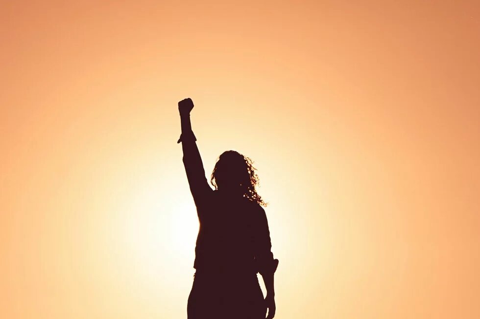 Foto: Silhouette einer Person mit erhobenem Arm vor einem Sonnenuntergang.
